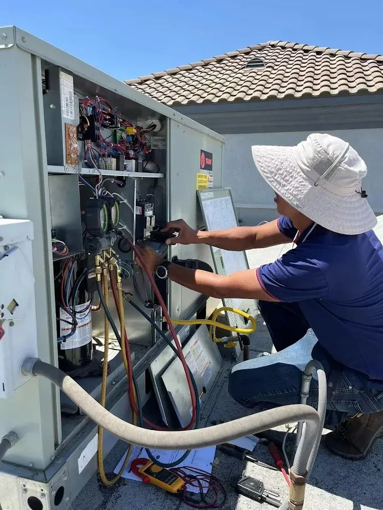 Technician repairing an HVAC unit on a rooftop under clear blue skies.